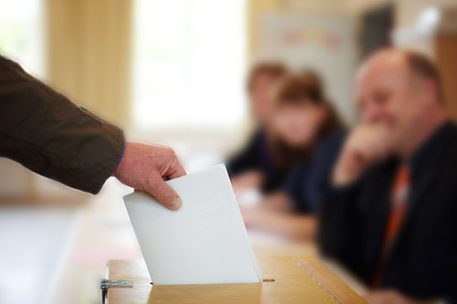 Stimmzettel wird in Wahlurne geworfen